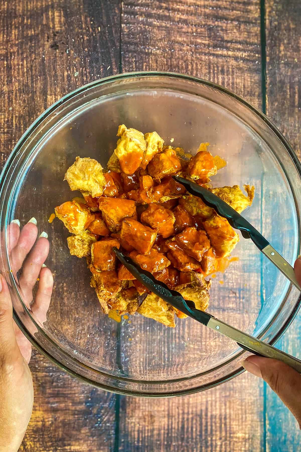 Tossing tofu chunks with vegan buffalo sauce.
